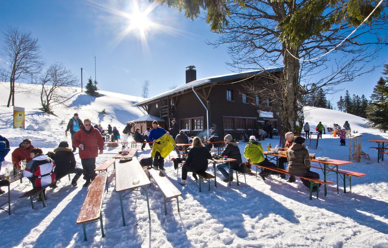 Auf Bierbänken lässt sich an der Krunkelbach-Hütte der strahlend blaue Wintertag bei einem Vesper genießen. Foto: Michael Arndt